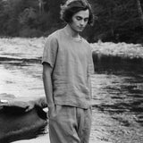 Person standing by a river wearing casual clothing, showcasing sustainable fashion and natural surroundings.