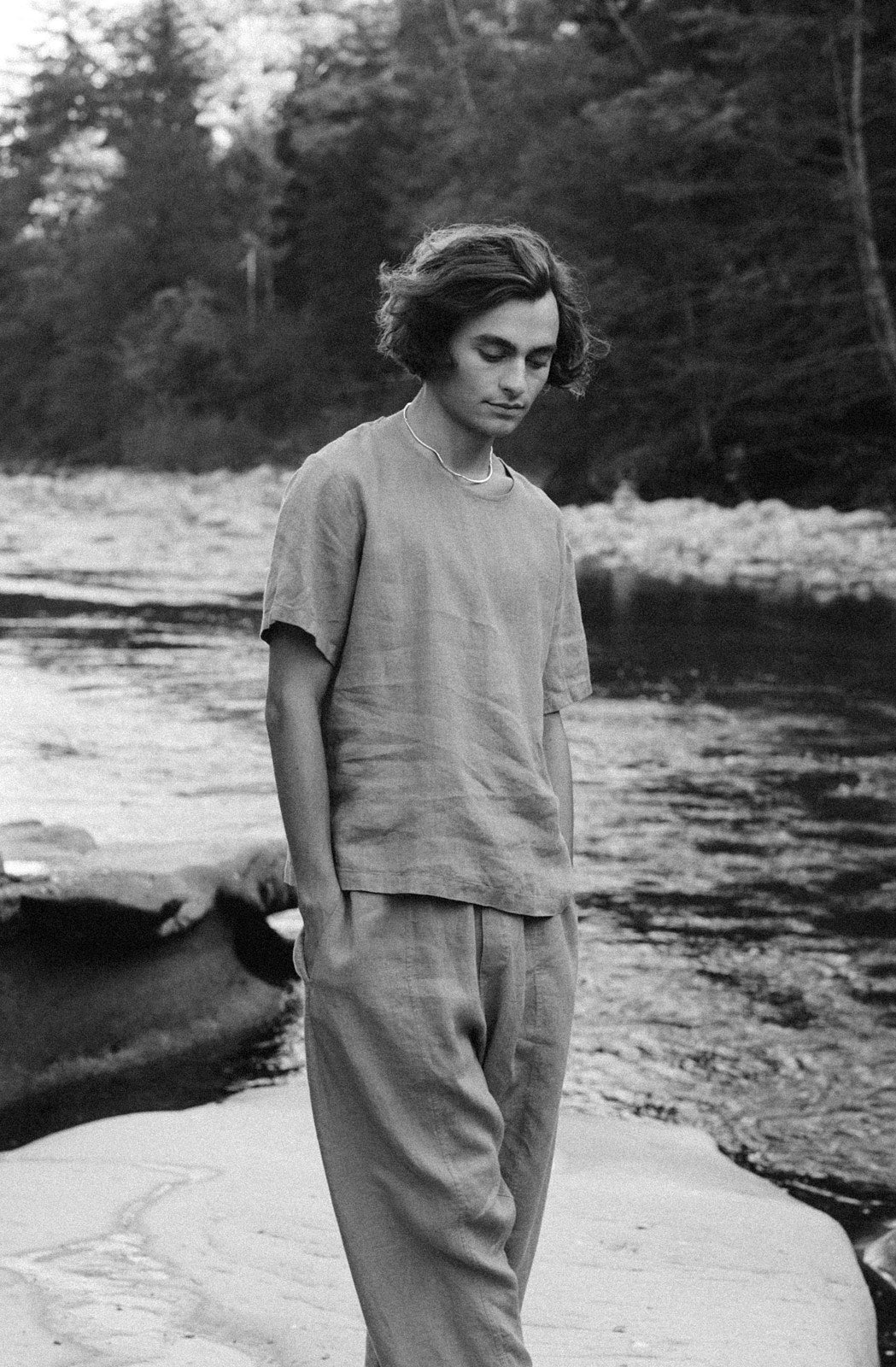 Person standing by a river wearing casual clothing, showcasing sustainable fashion and natural surroundings.