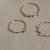Three handcrafted rings made of 18k recycled gold, showcasing organic designs, on a soft beige background.