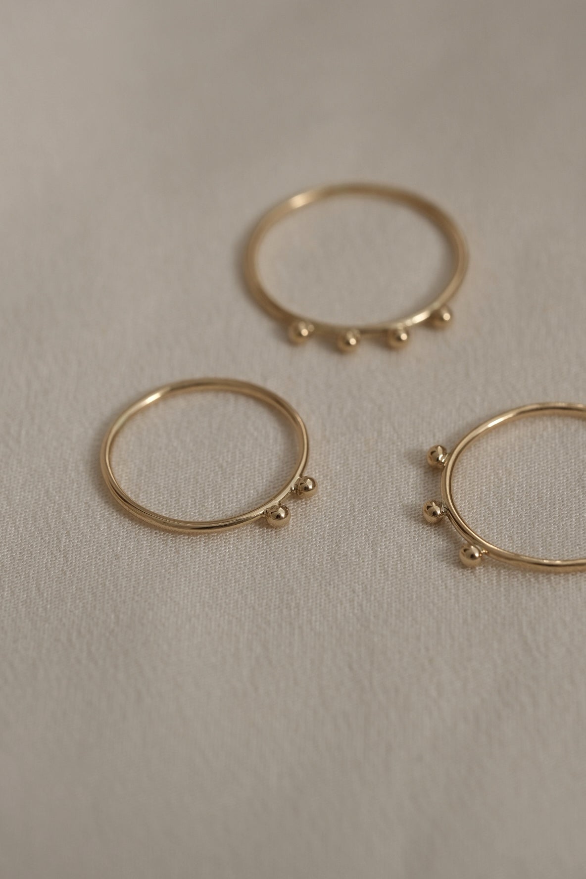 Three handcrafted rings made of 18k recycled gold, showcasing organic designs, on a soft beige background.