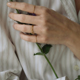 Hand wearing handcrafted 18k recycled gold rings, holding a flower, styled in a casual shirt from Basel, Switzerland.