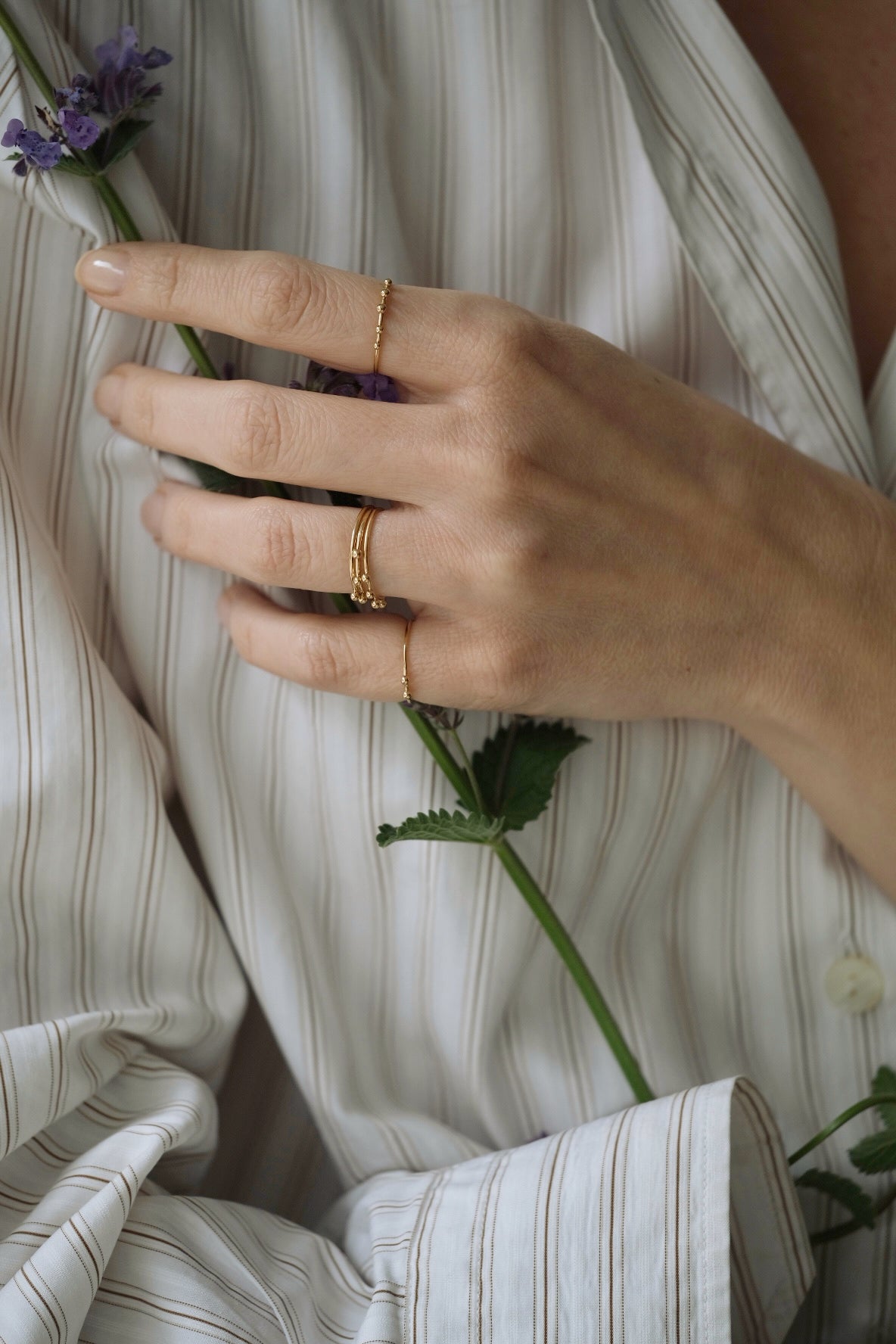 Hand wearing handcrafted 18k recycled gold rings, holding a flower, styled in a casual shirt from Basel, Switzerland.