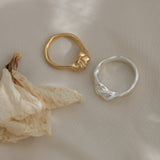 Two handmade unique rings: a gold-plated and a silver ring, against a textured background with dried petals.