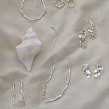 Handmade ethical jewelry collection featuring silver rings, earrings, necklace, and a seashell on a soft surface.