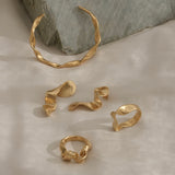 Unique handmade gold rings and cuff bracelet on textured background, showcasing ethical and sustainable jewelry.