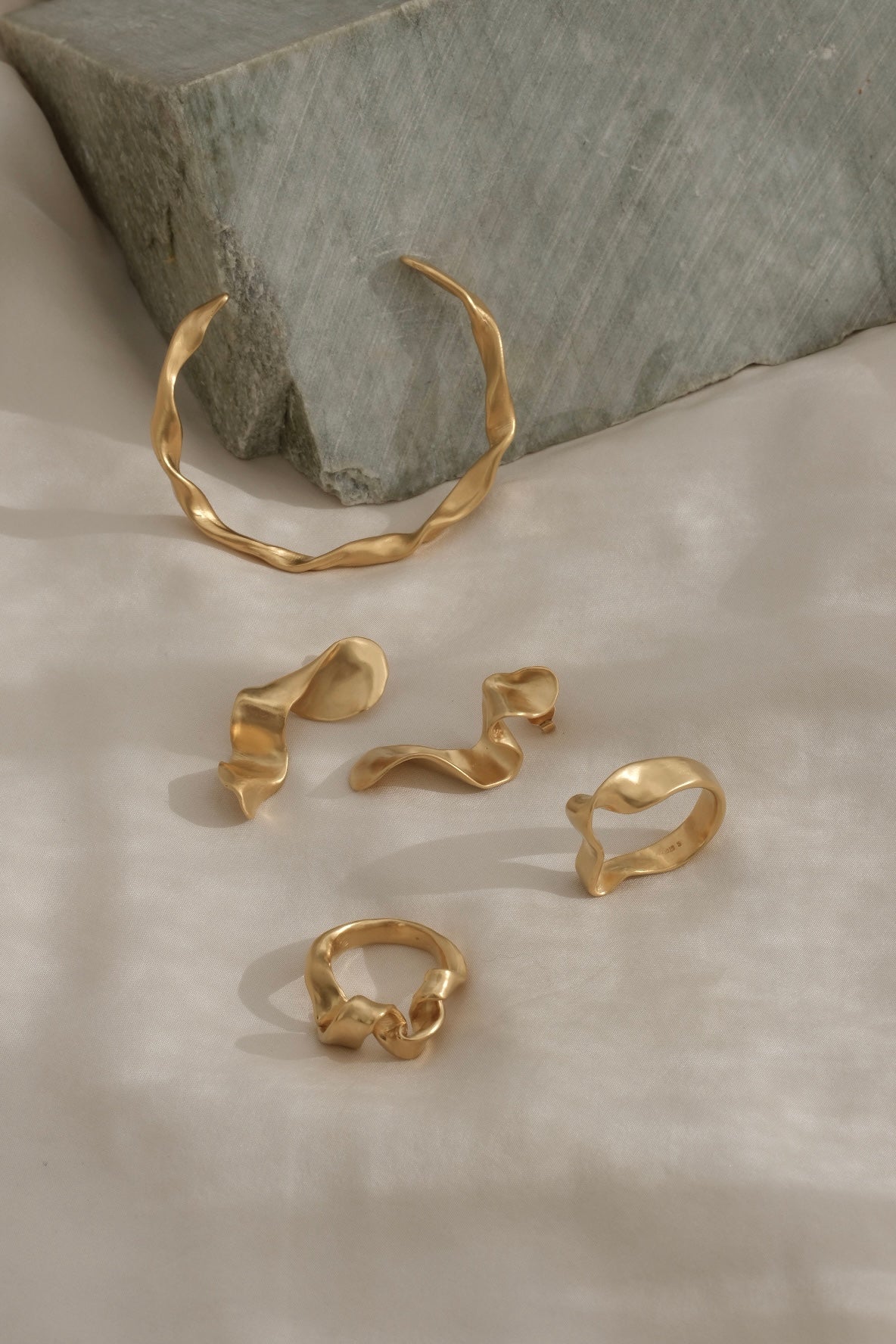 Unique handmade gold rings and cuff bracelet on textured background, showcasing ethical and sustainable jewelry.