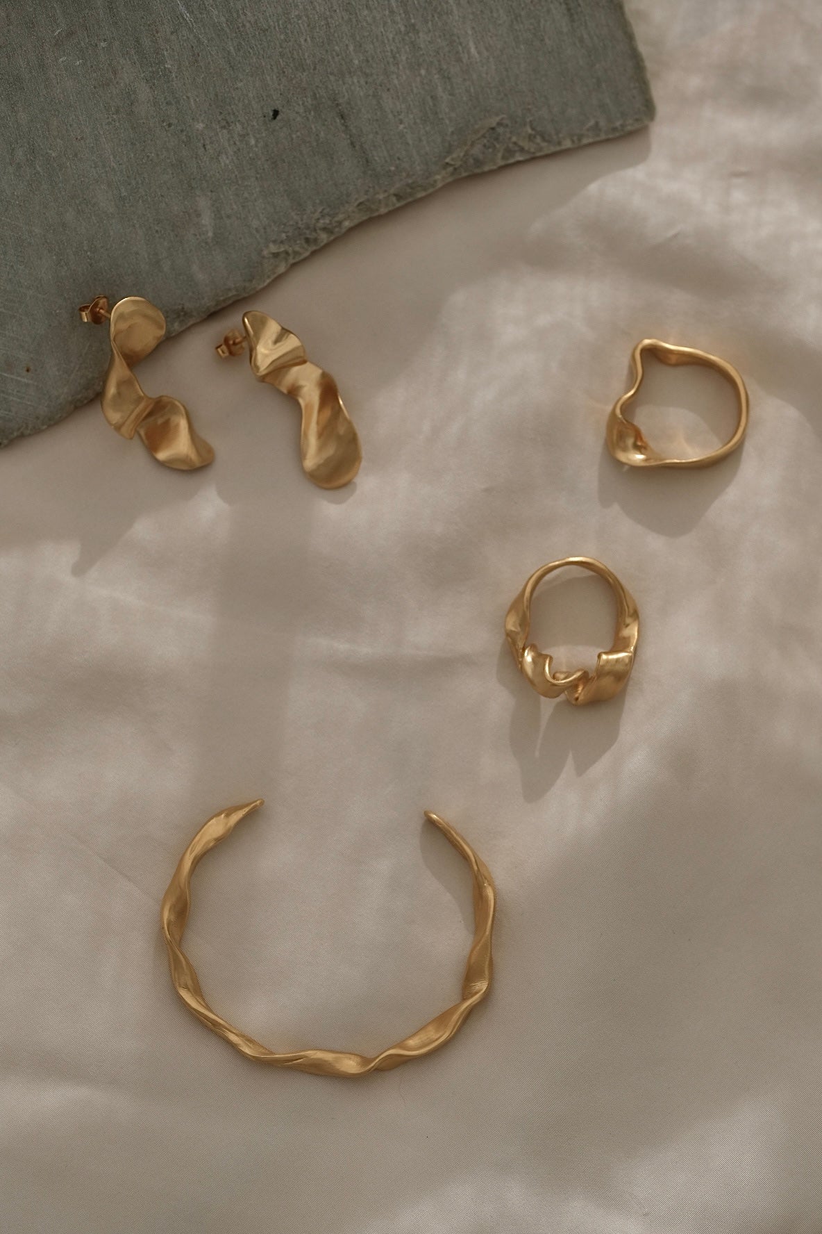 Handmade ethical and sustainable jewelry featuring gold-plated earrings and rings on soft fabric backdrop.