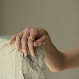 Hand showcasing DROP 01 ring, made of ethical 18k gold-plated recycled silver, in a serene setting.