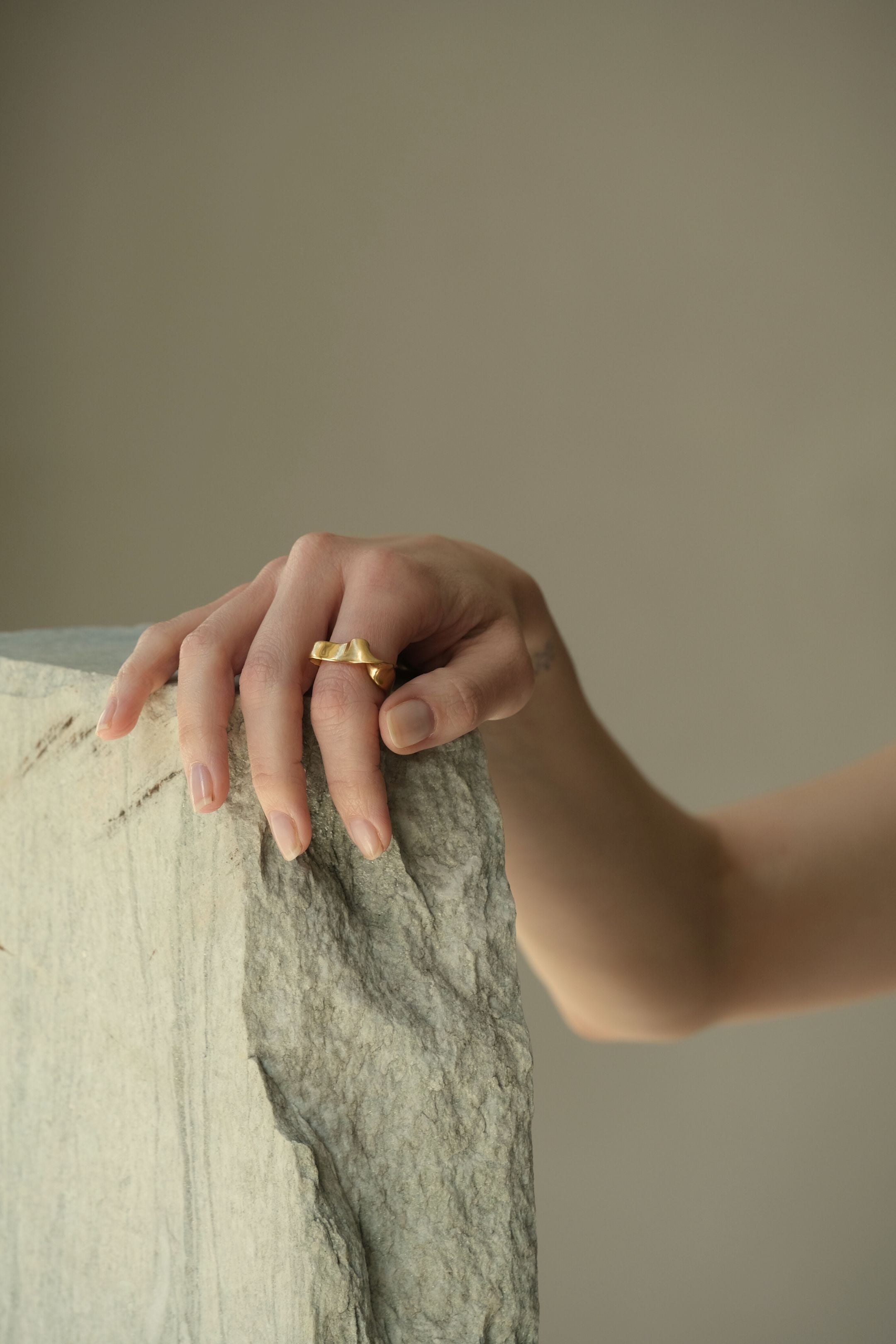 Hand showcasing DROP 01 ring, made of ethical 18k gold-plated recycled silver, in a serene setting.