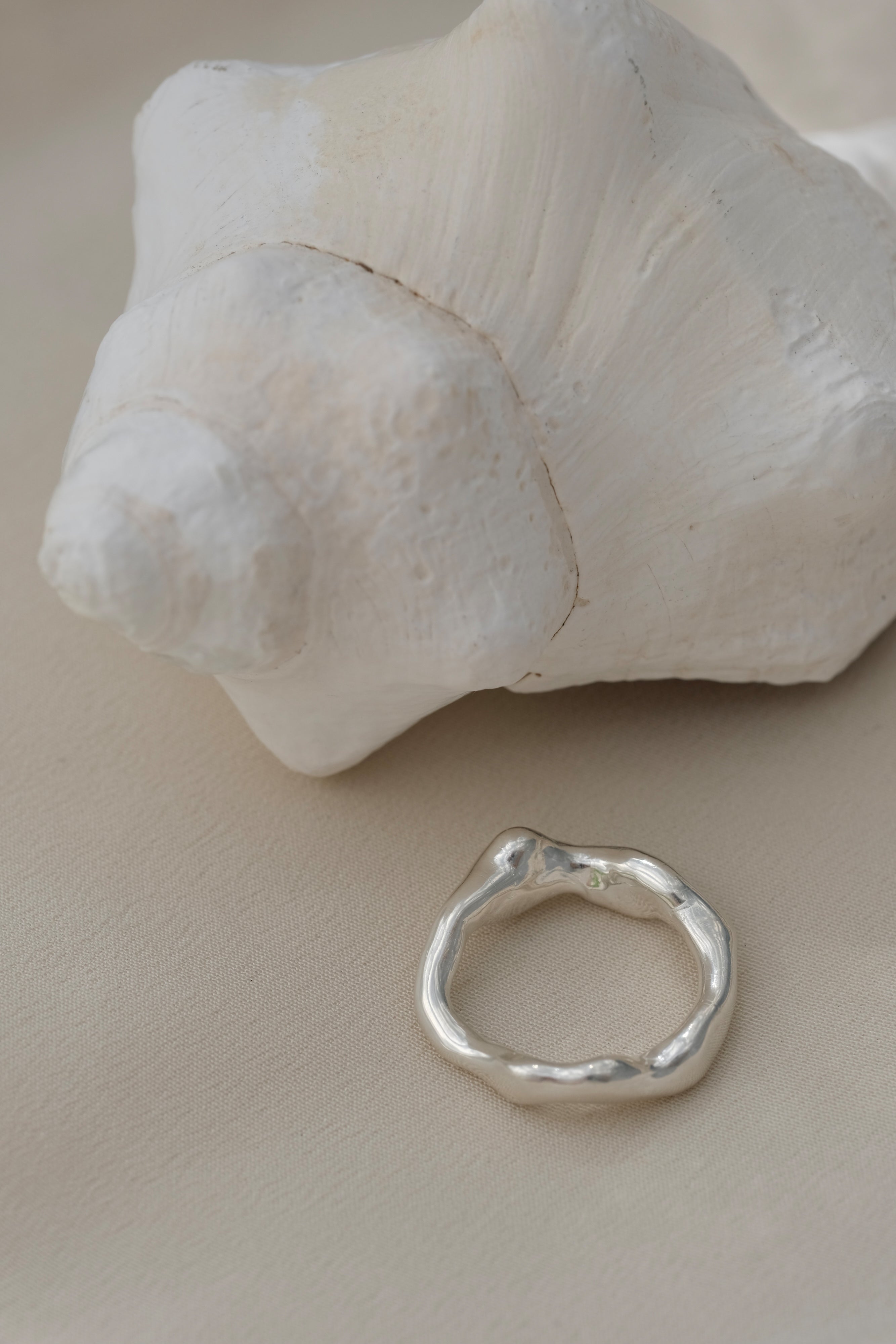 Handmade ring in 925 recycled silver next to a seashell, showcasing unique, ethical jewelry from Basel, Switzerland.