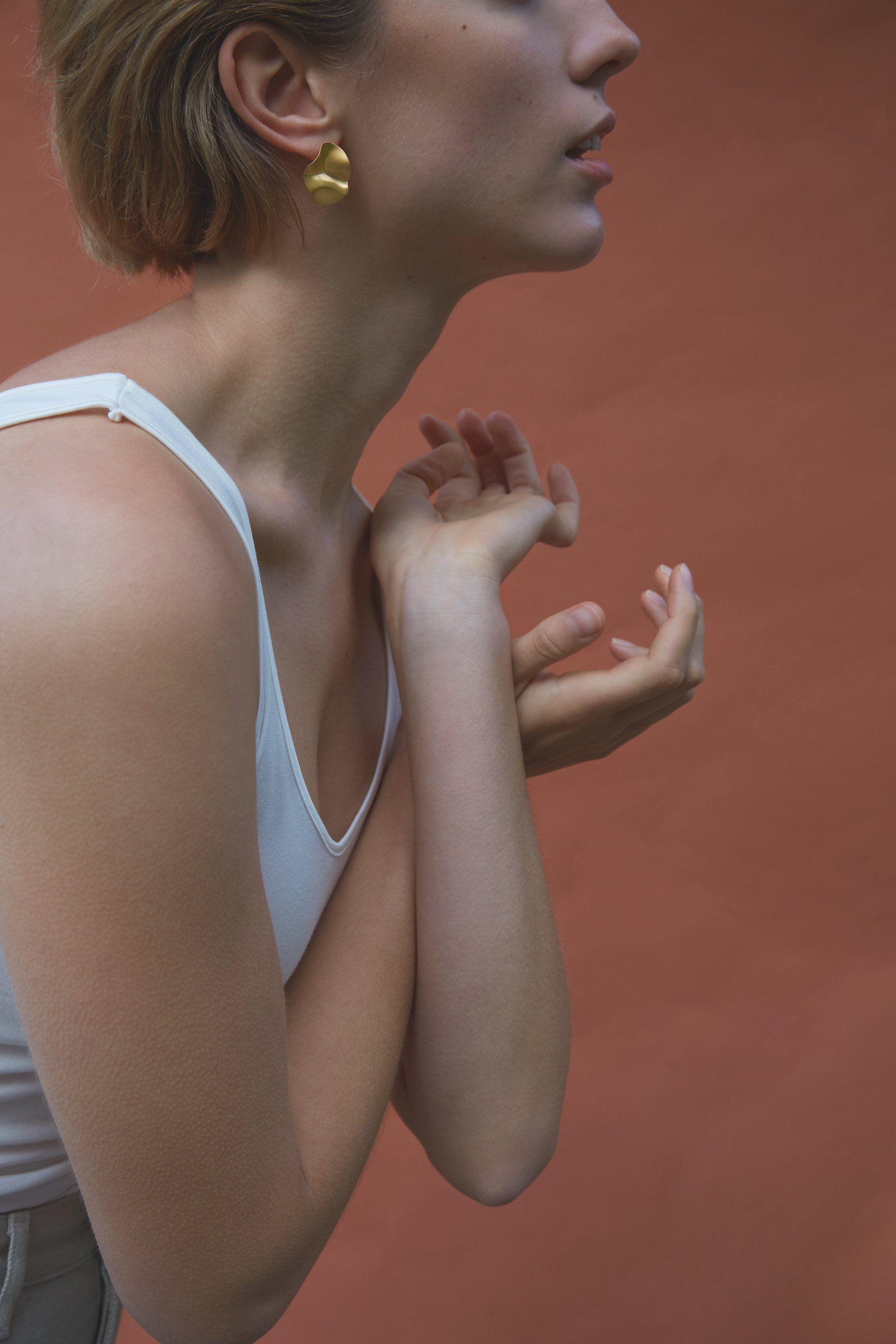 Model wearing AROYO small earrings, showcasing handmade ethical jewelry with a semi-matte finish against a warm backdrop.
