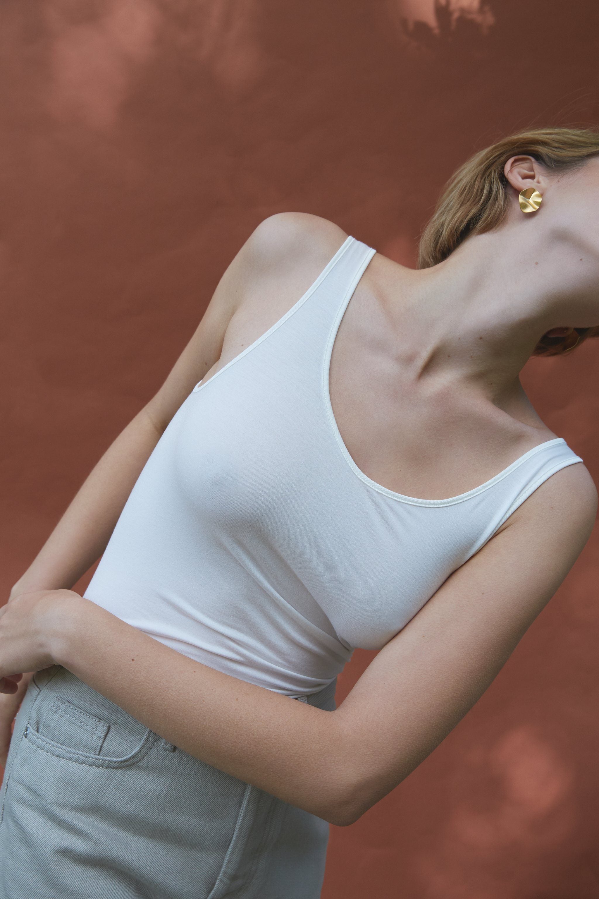 Model wearing AROYO small earrings with a white tank top against a warm, earthy background.