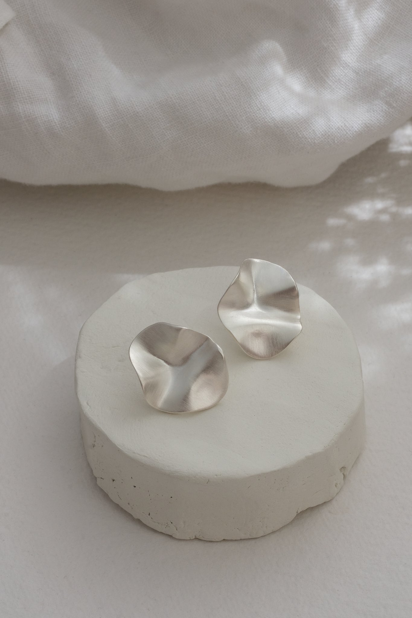 Handmade AROYO small earrings made of recycled silver in a semi-matte finish, displayed on a minimalist stand.