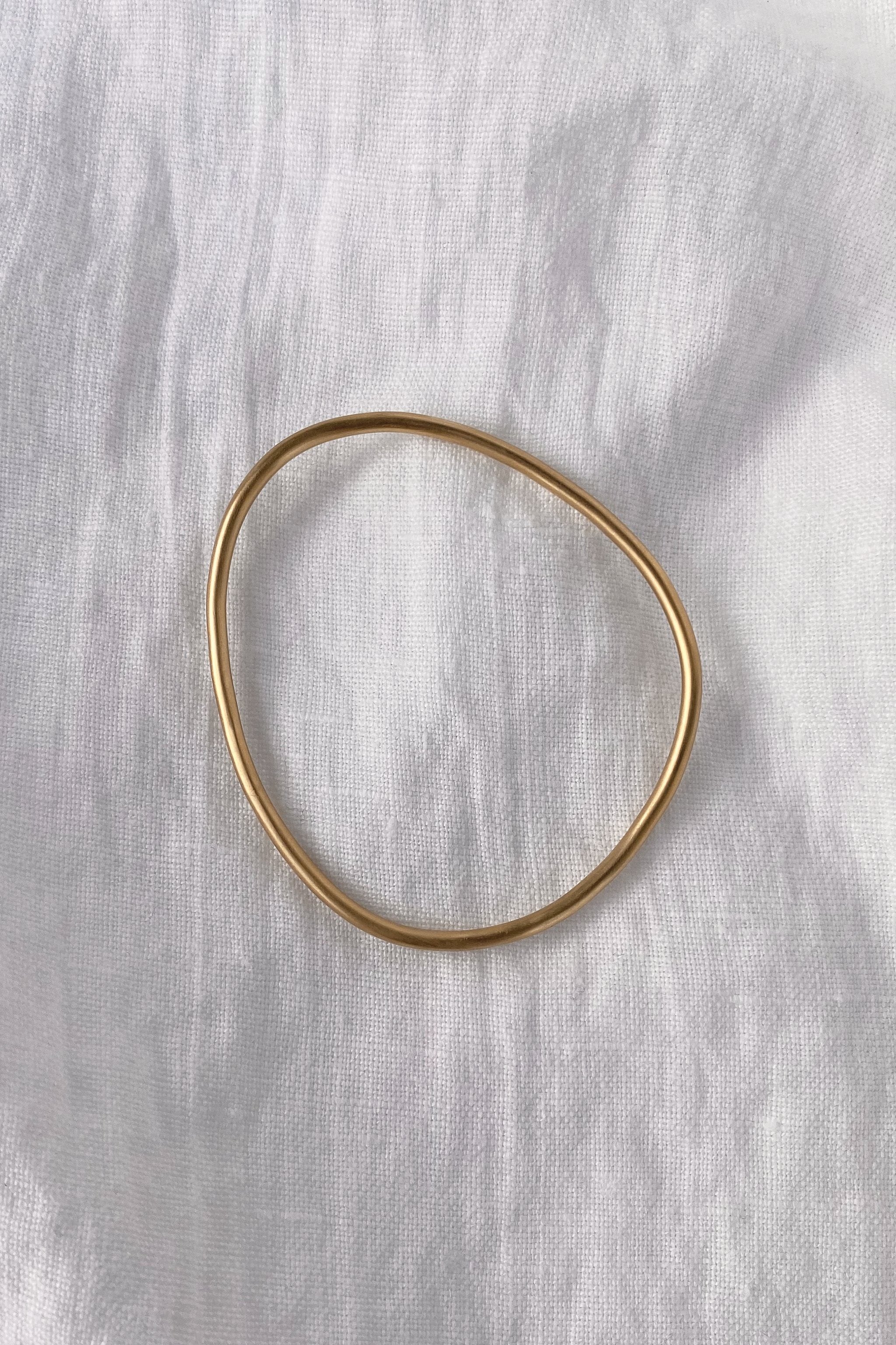 LOON bangle made of 18k gold-plated recycled silver, showcasing a handmade, semi-shiny finish on a white linen background.