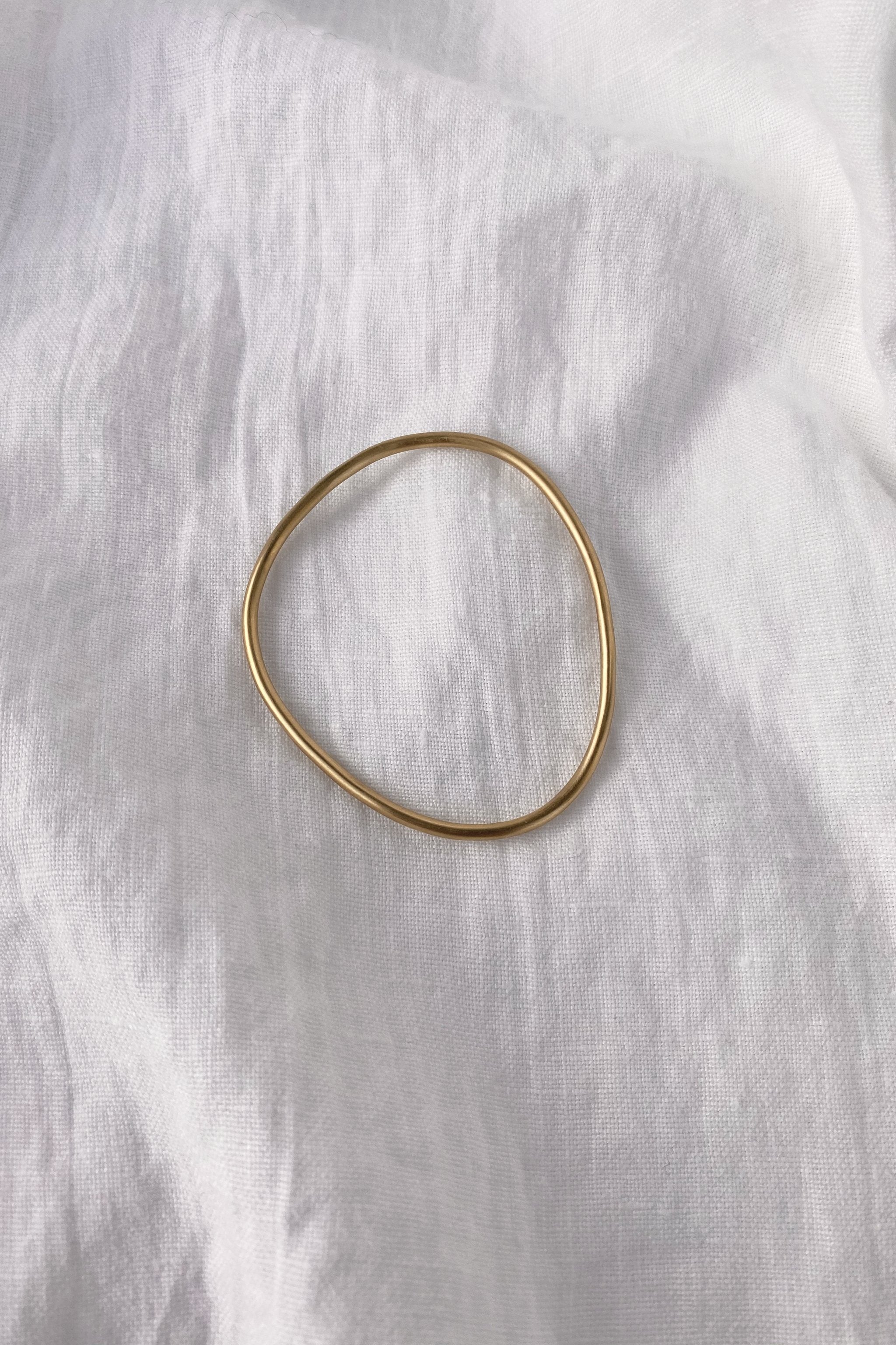 Handmade LOON bangle in 18k gold-plated recycled silver on white fabric, a piece of ethical and sustainable jewelry.