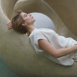 Model lounging in a sculptural chair, showcasing LOON big earrings made from recycled silver for ethical jewelry.