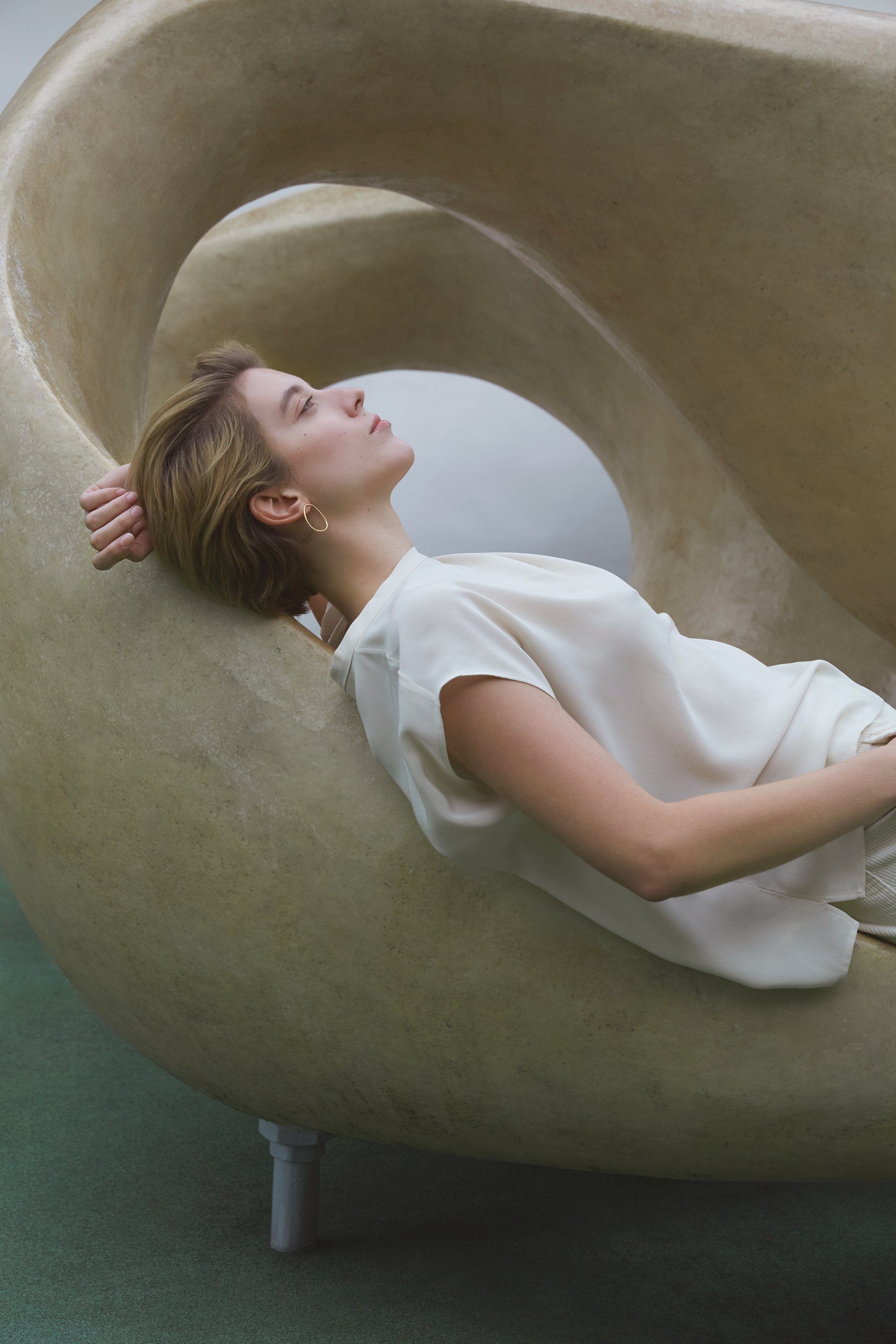 Model lounging in a sculptural chair, showcasing LOON big earrings made from recycled silver for ethical jewelry.