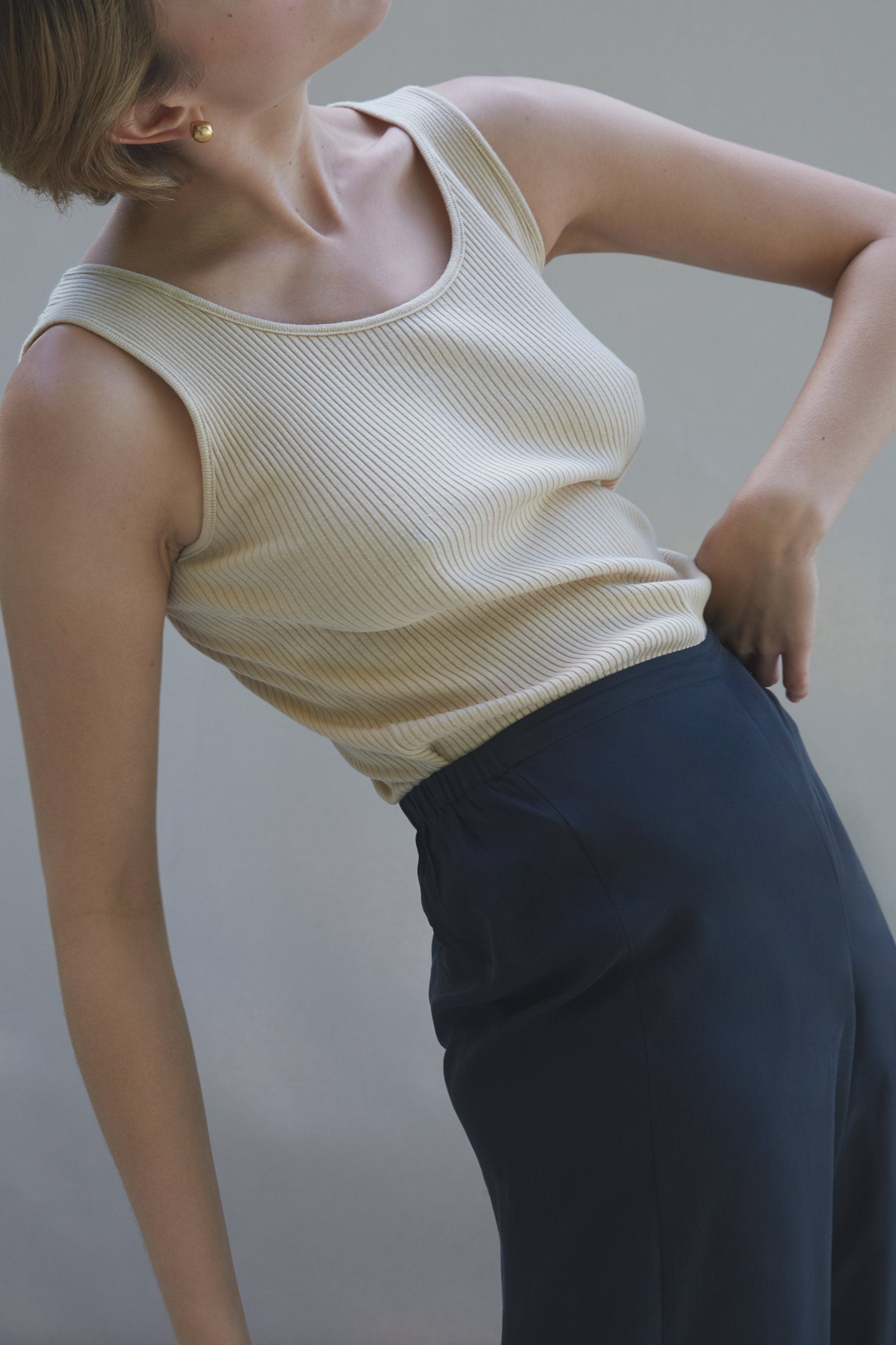 Model wearing a ribbed beige tank top paired with high-waisted navy trousers, showcasing a trendy outfit.