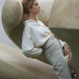 Model wearing a stylish white blouse and beige pants, posed against a sculptural backdrop, showcasing modern fashion design.