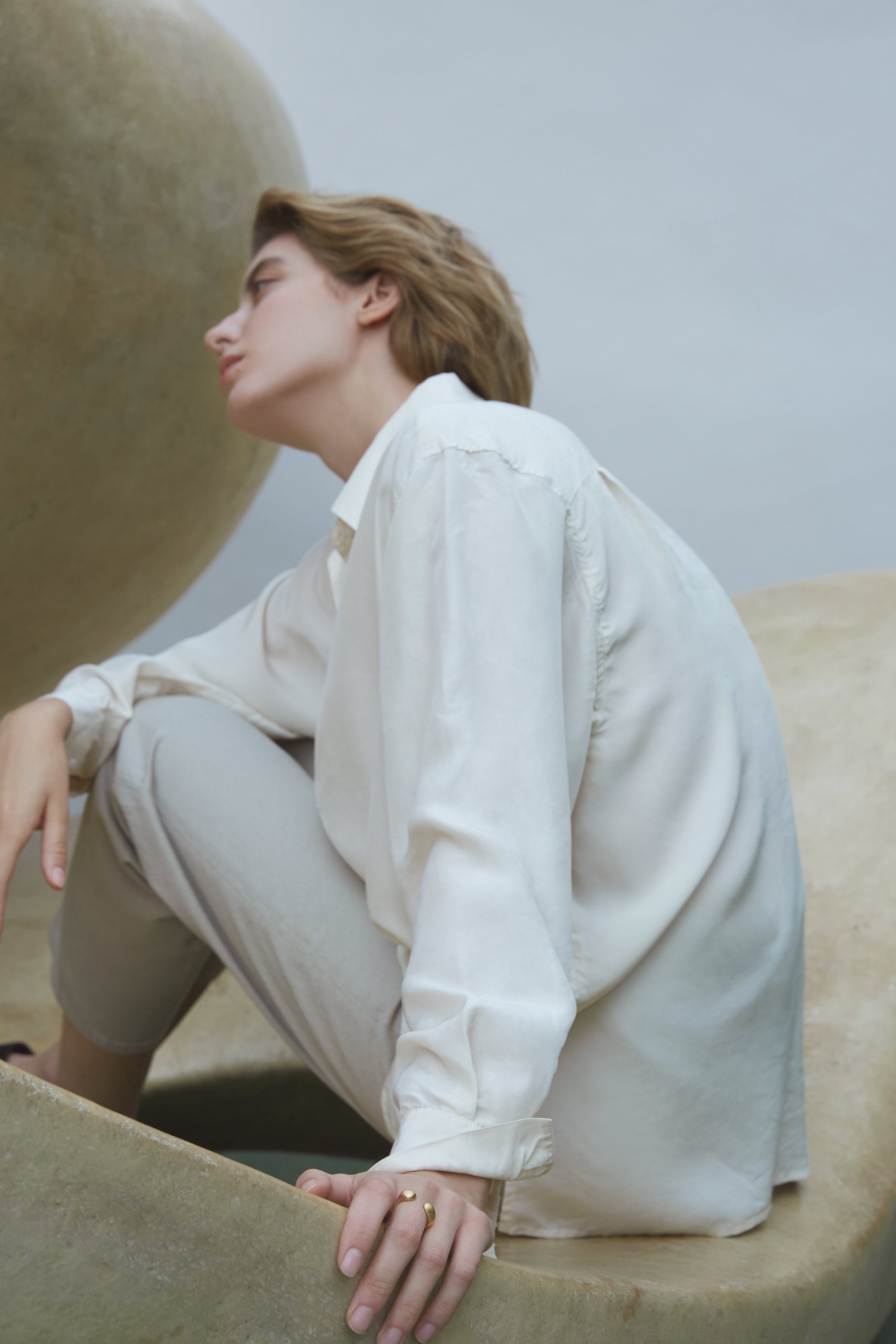 Model wearing a white shirt and light pants, showcasing the handmade ONOA ring in an artistic setting.