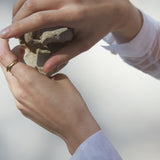 Hands holding a stone, adorned with YERERA big ring, showcasing ethical and sustainable jewelry craftsmanship.