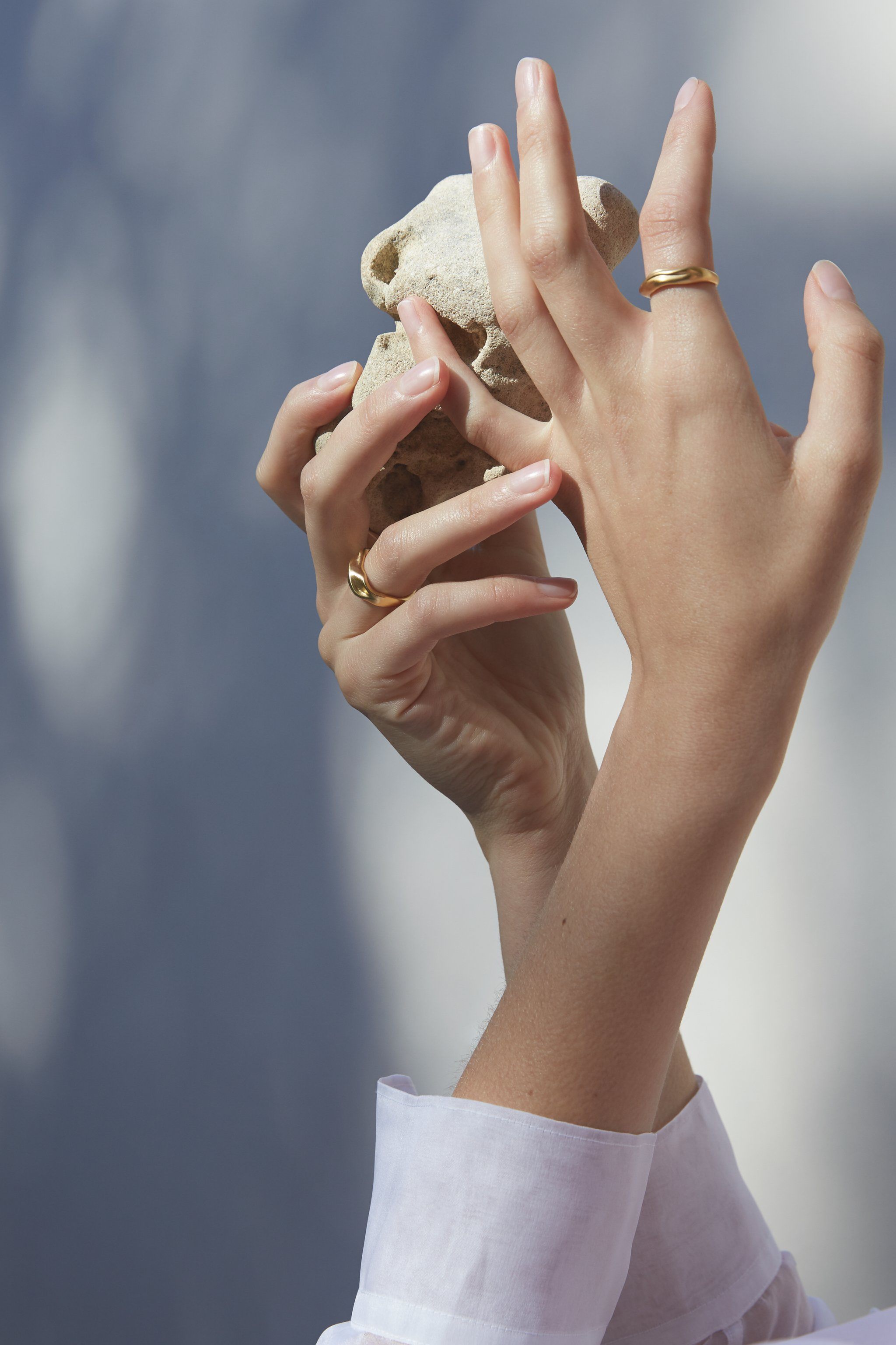 Hands holding a natural stone wearing YERERA small ring, showcasing ethical handmade jewelry in gold-plated brass.