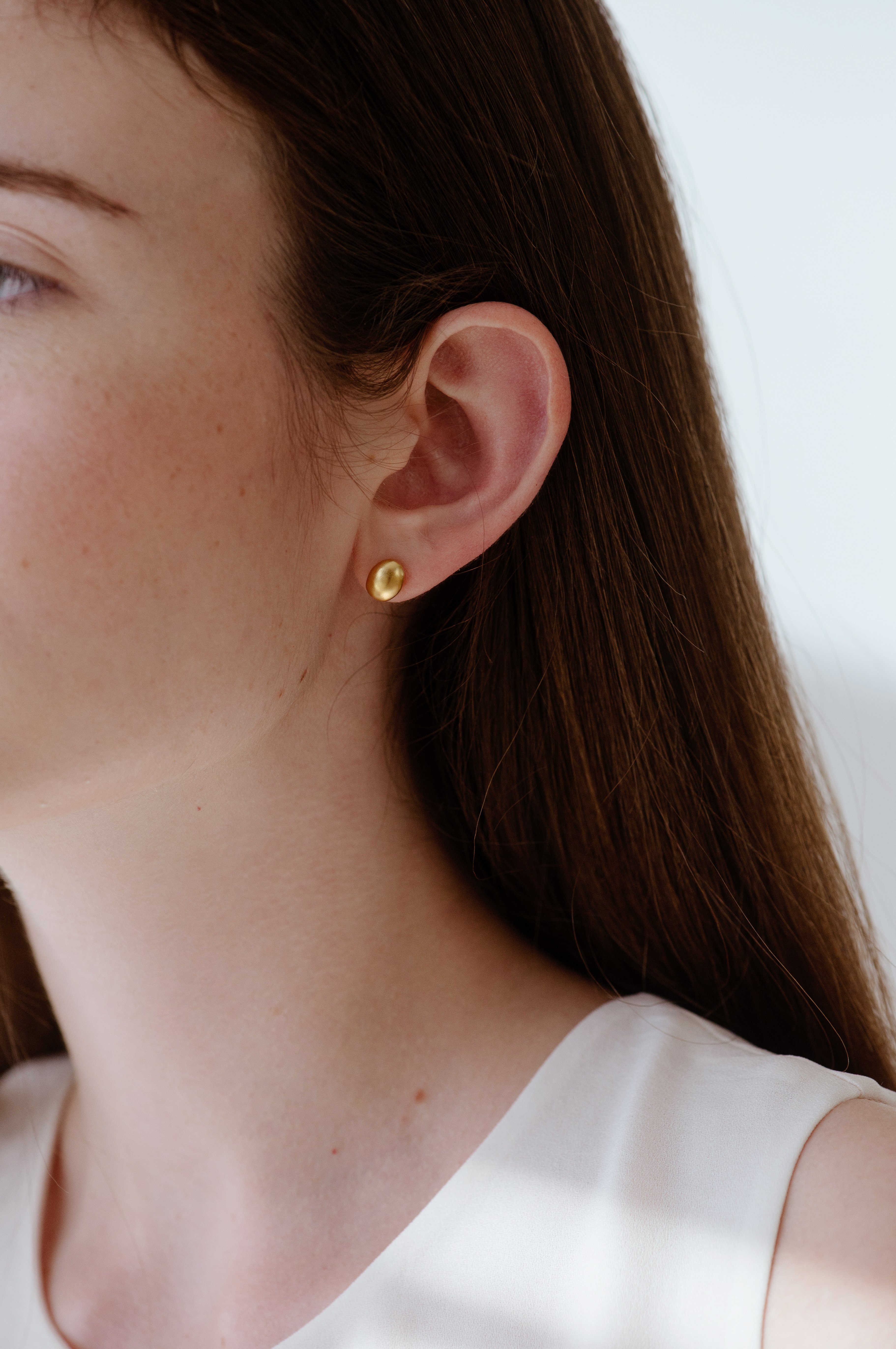 Close-up of a woman wearing PEBBLE earrings, handmade ethical jewelry in 18k gold-plated recycled silver.