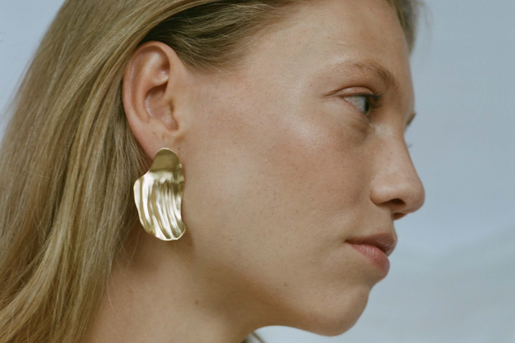 Handmade AJUN earrings in recycled gold, showcasing a matte finish on a model's ear, highlighting ethical jewelry design.