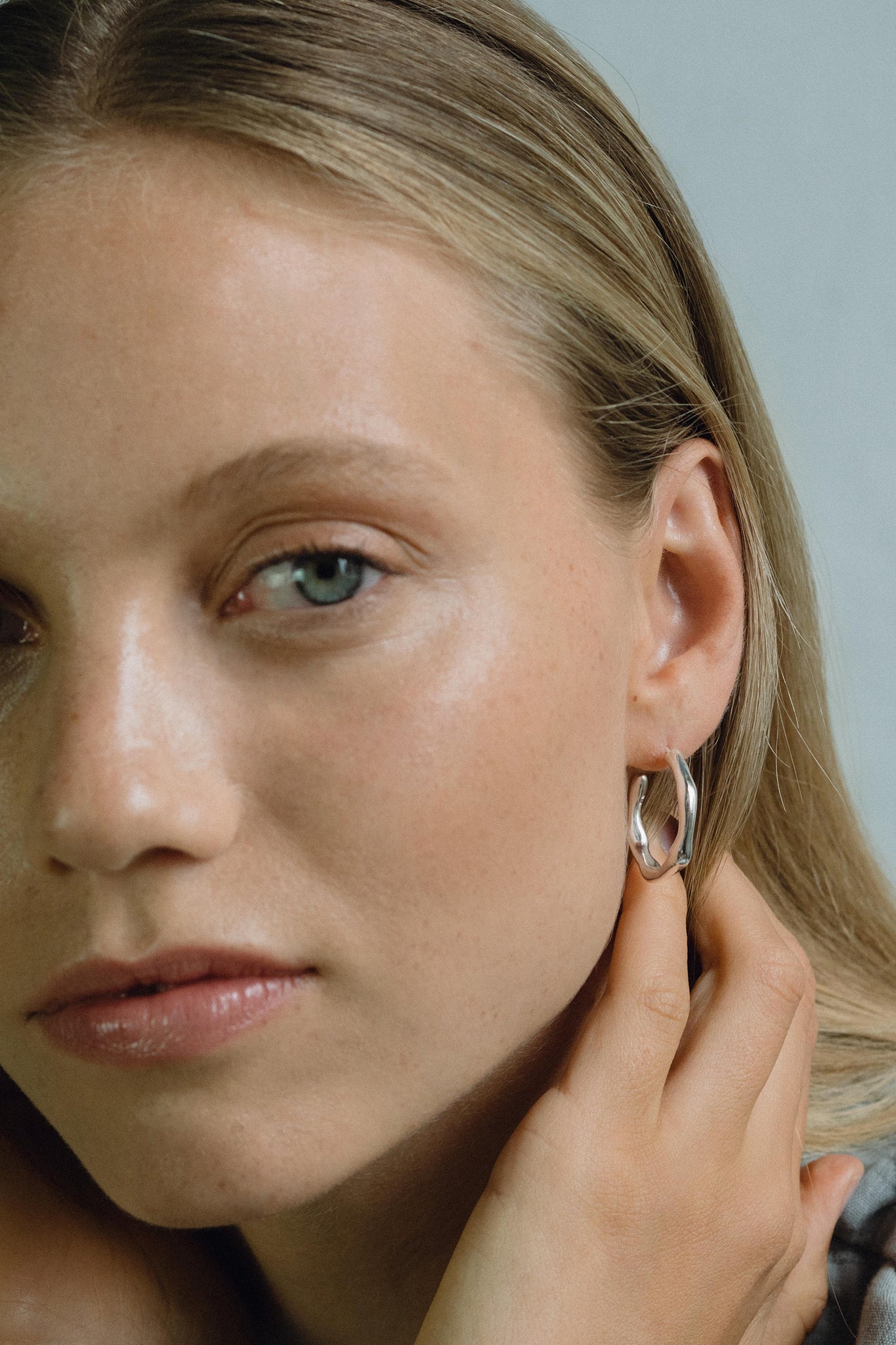 Close-up of a woman wearing LUMI big handmade earrings made from recycled silver, showcasing ethical jewelry design.