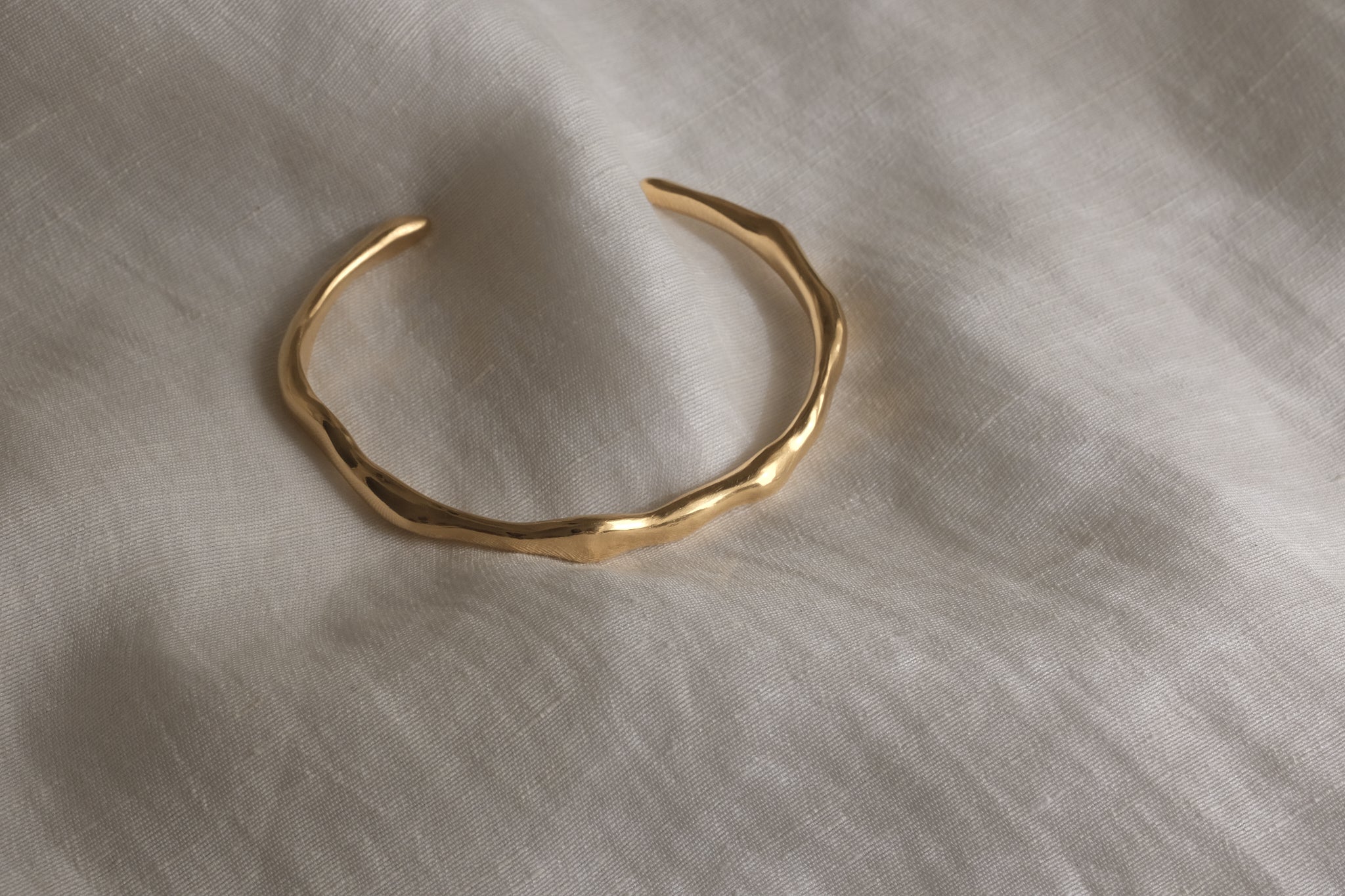 LUMI cuff made of 18k gold-plated recycled silver, showcasing a handmade, ethical design on a soft fabric background.