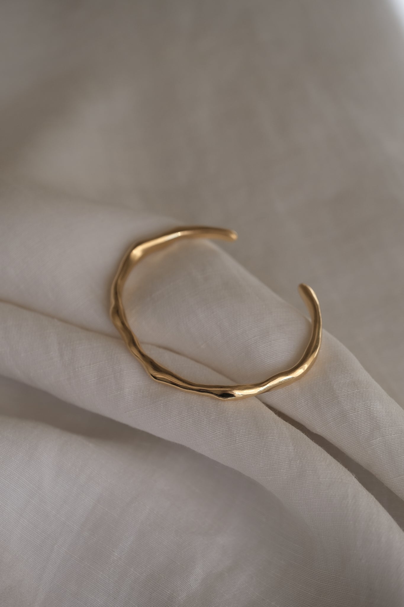 LUMI cuff in 18k gold-plated recycled silver, showcasing sustainable and handmade ethical jewelry on soft fabric.