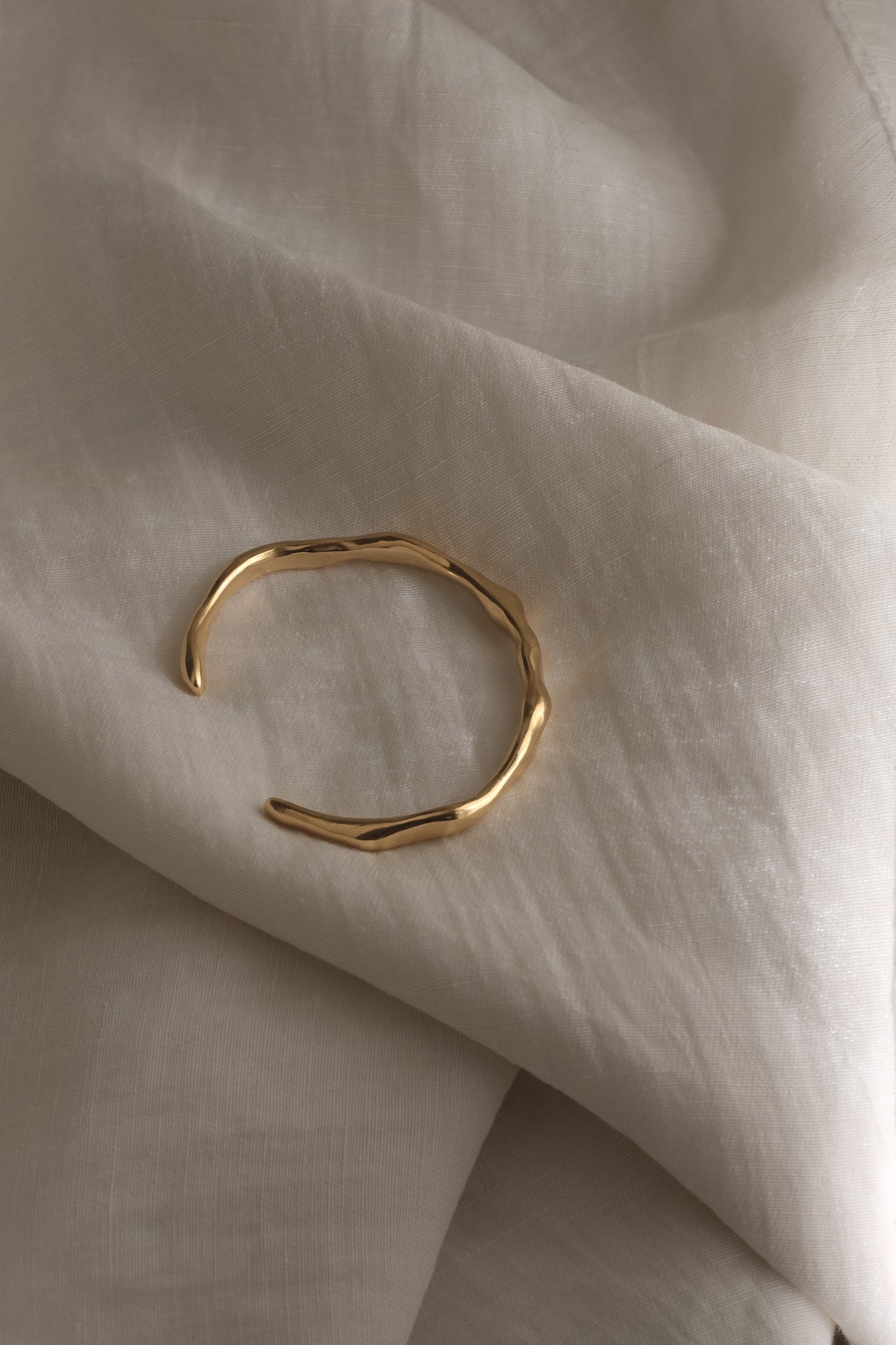 LUMI cuff bracelet in 18k gold-plated recycled silver resting on soft fabric, showcasing sustainable handmade ethical jewelry.