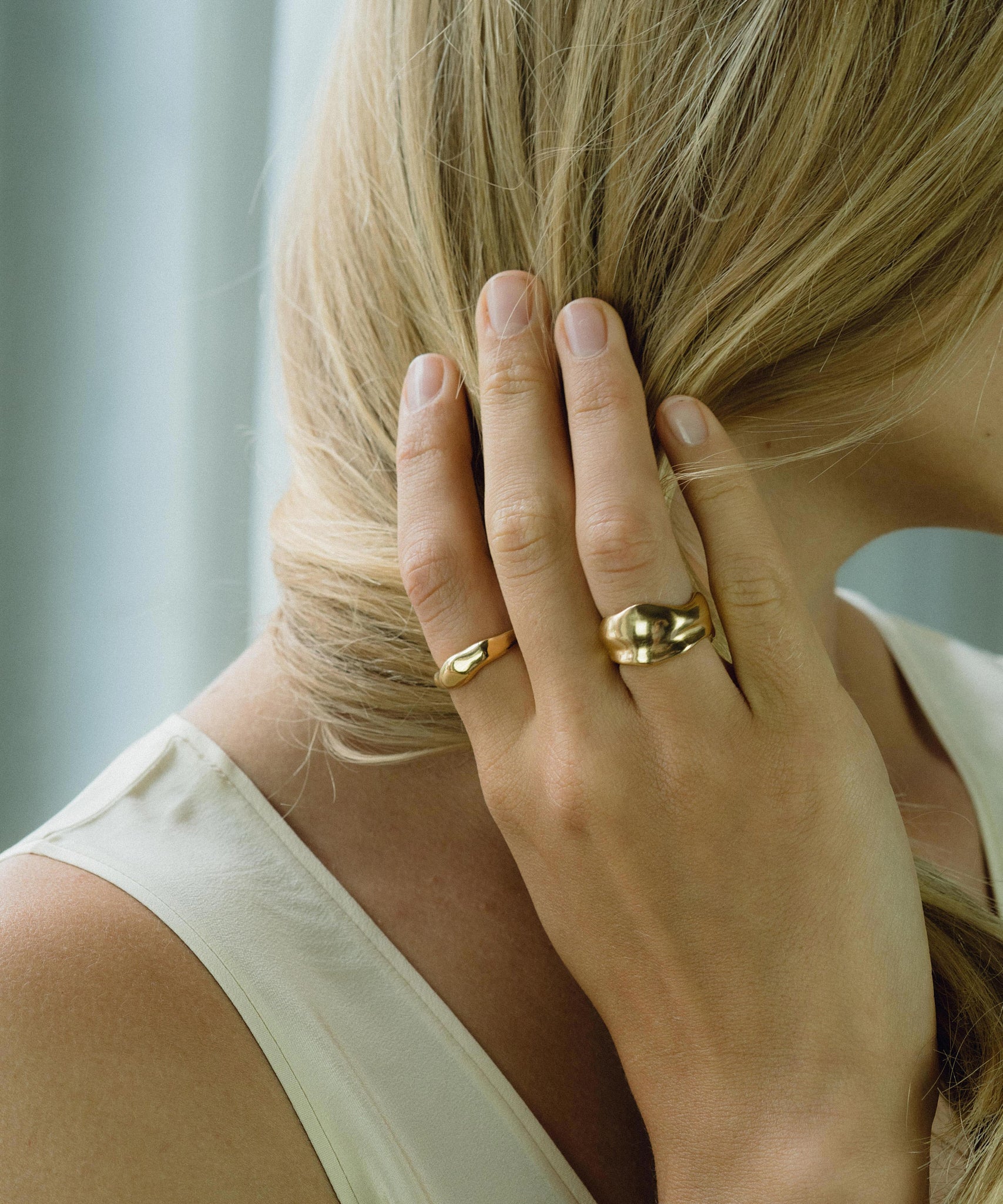 Close-up of a hand with two ethical handmade rings, showcasing sustainable 18k gold-plated recycled silver jewelry.