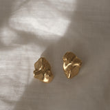Handmade MOA earrings in 18k gold-plated recycled silver, showcasing a natural shiny surface on a soft fabric backdrop.
