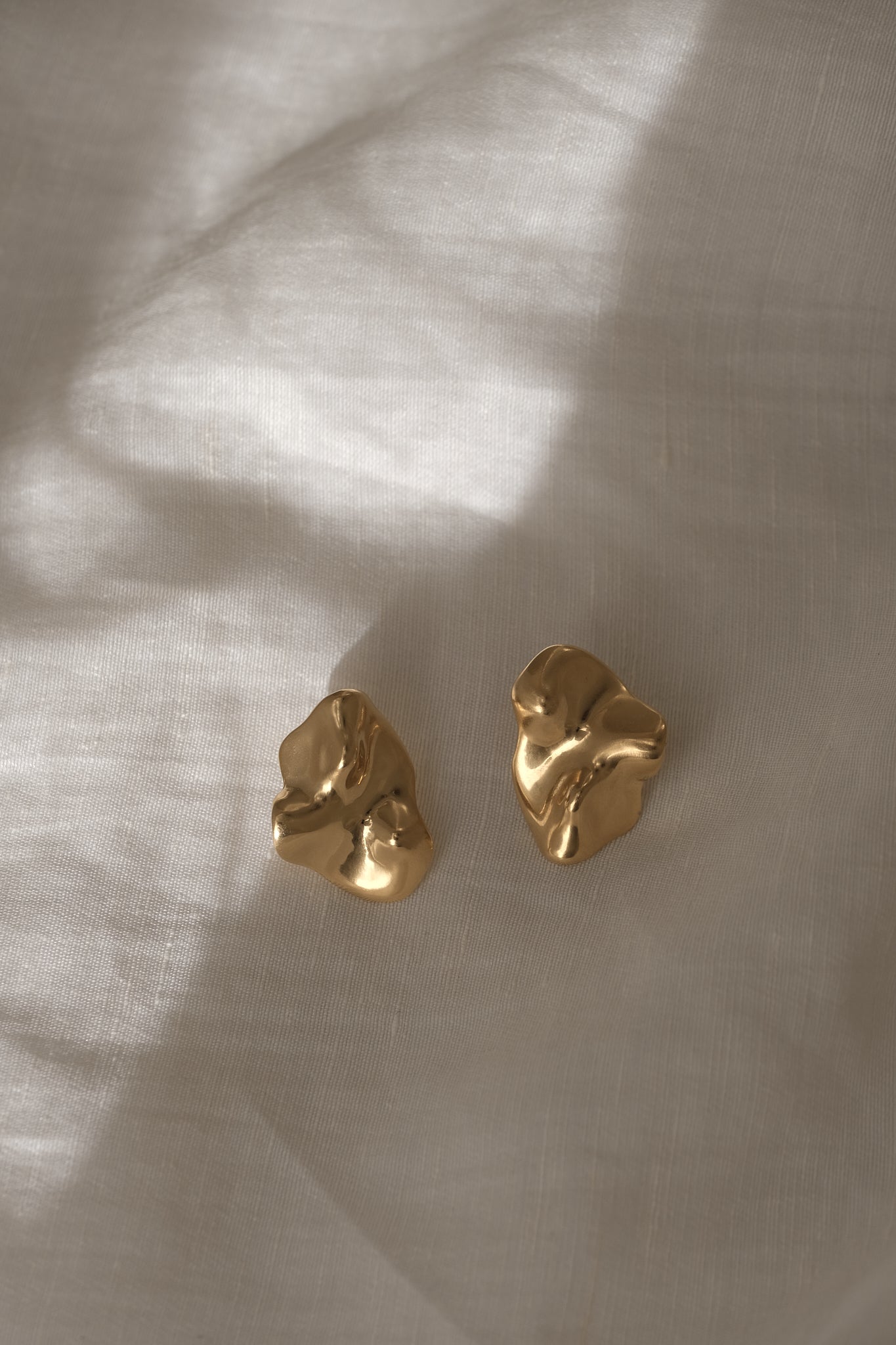 Handmade MOA earrings in 18k gold-plated recycled silver, showcasing a natural shiny surface on a soft fabric backdrop.