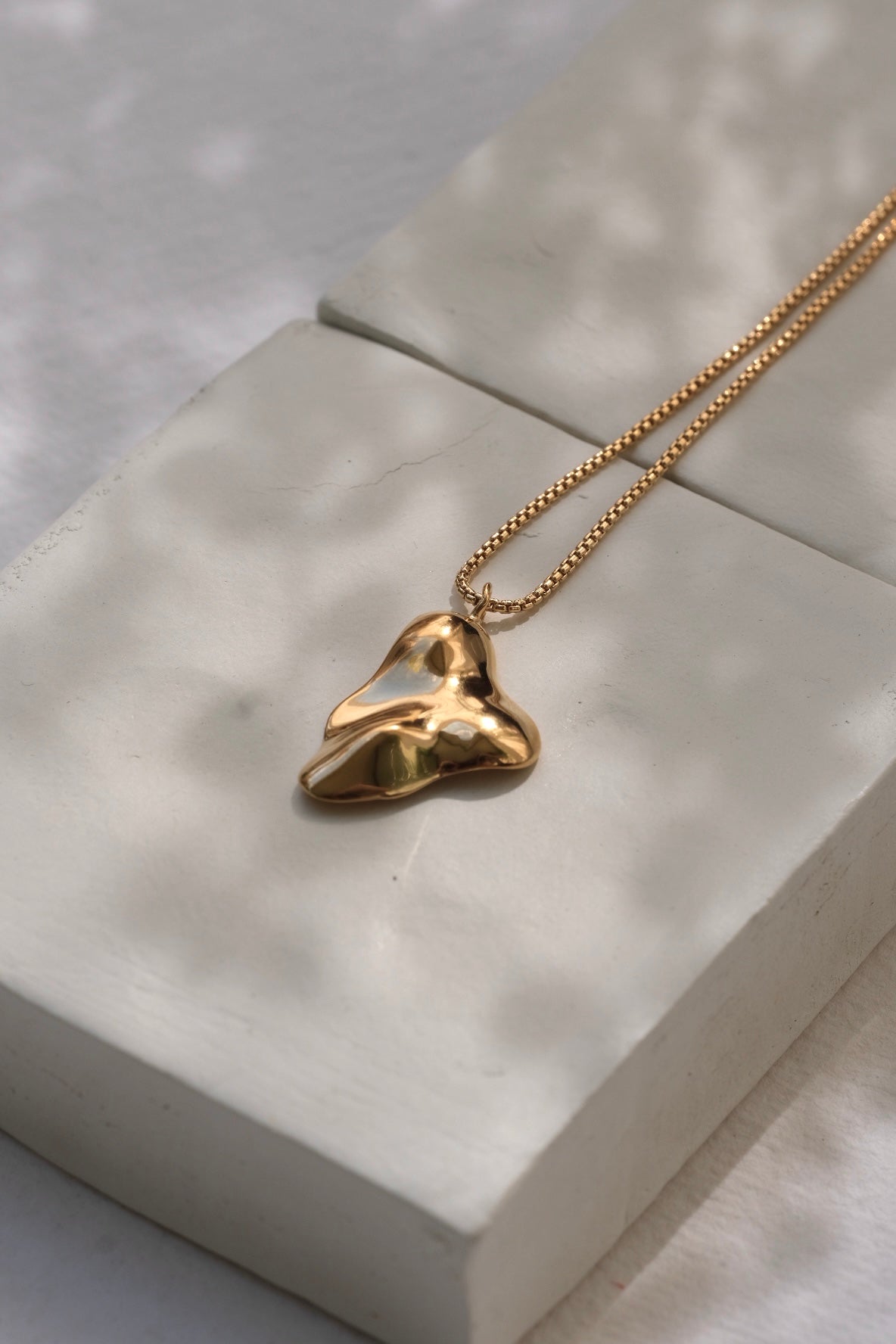 Handmade MOA necklace in 18k recycled gold on a minimalist display, showcasing sustainable and ethical jewelry.