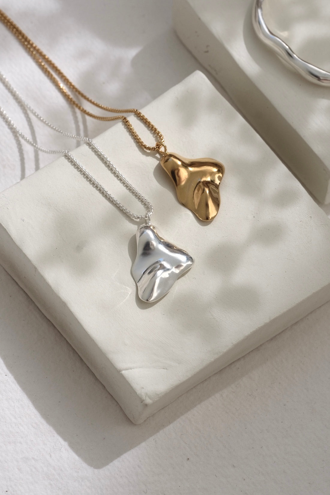 Handmade MOA necklace featuring 18k gold-plated and recycled silver pendants on a display showcasing ethical jewelry.