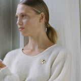 Model showcasing handmade 18k gold-plated MOA brooch on a cozy white sweater, highlighting ethical jewelry.