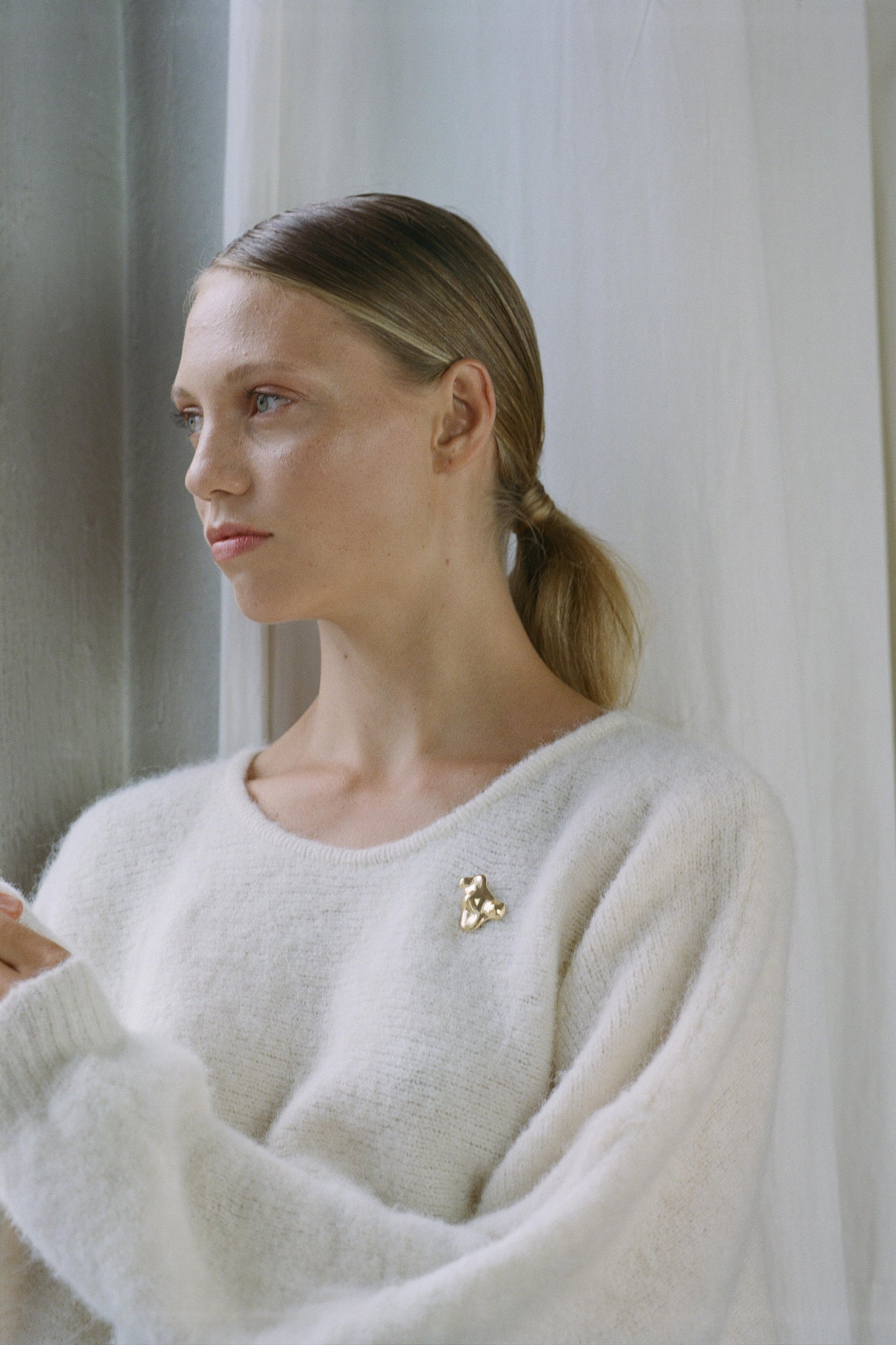 Model showcasing handmade 18k gold-plated MOA brooch on a cozy white sweater, highlighting ethical jewelry.