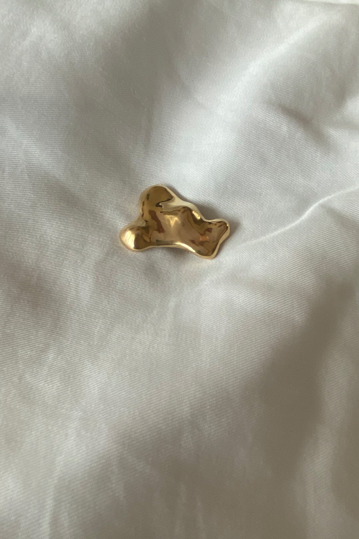 Handmade MOA brooch in 18k gold-plated recycled silver, featuring a natural shiny surface, on a soft fabric background.